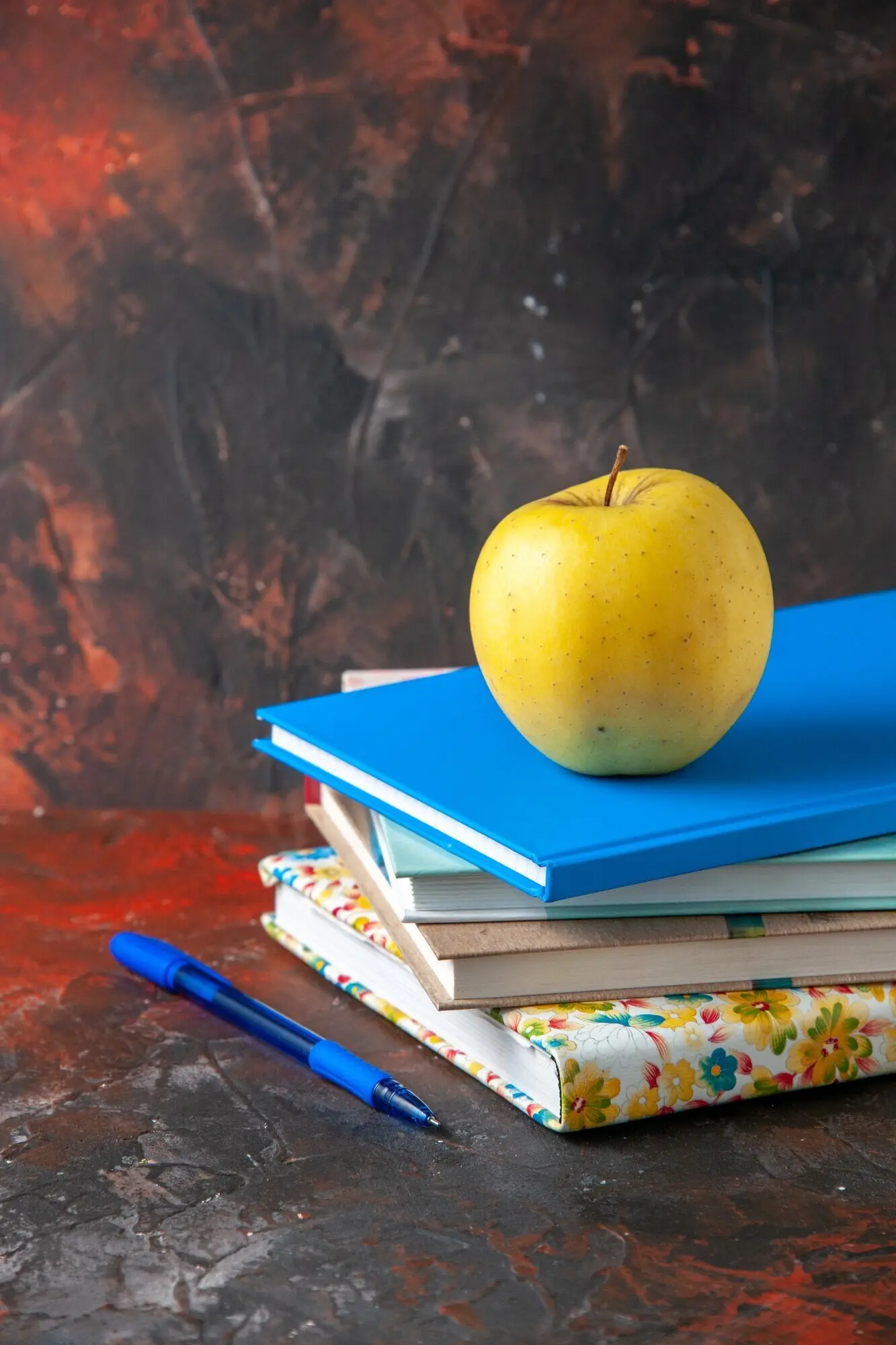 Vertikale Ansicht eines frischen gelben Apfels auf gestapelten Notizbüchern auf der linken Seite vor dunklem Hintergrund.